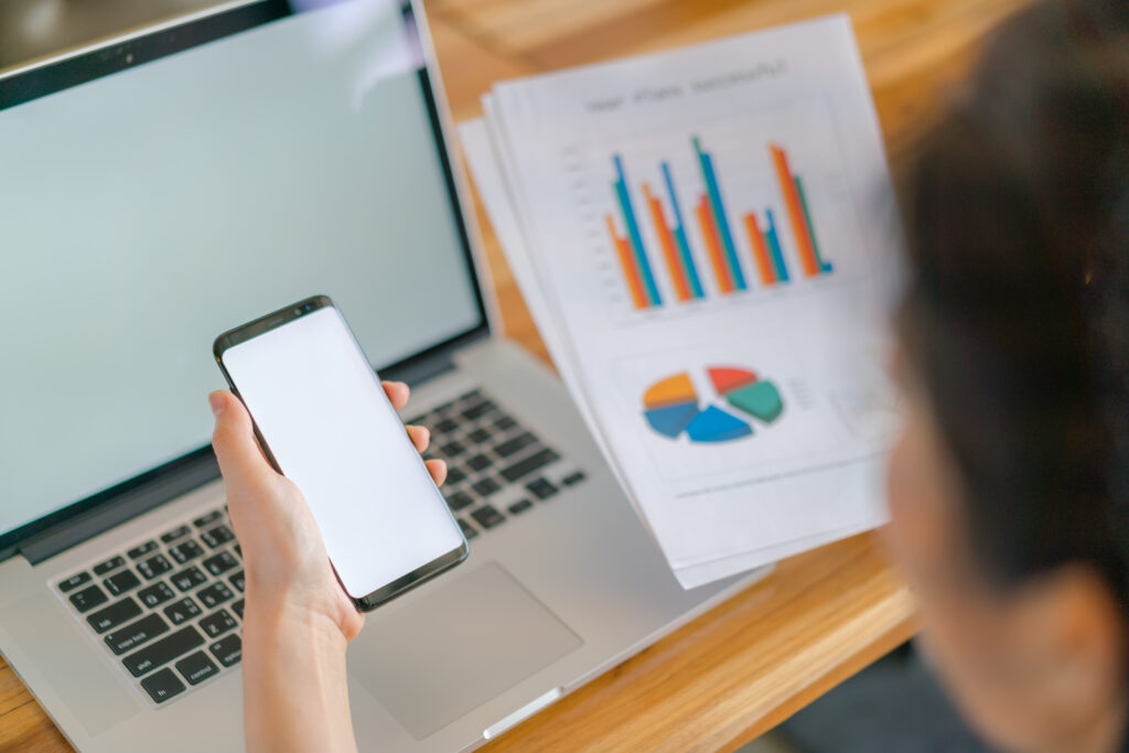 Business woman hand with Financial charts and mobile phone over laptop on the table